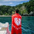 Person on a boat wearing a red towel with New Zealand branding, looking at a scenic island.
